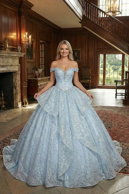 Light blue layered ruffled ball gown with off-shoulder design and embroidery, worn in an elegant mansion setting.