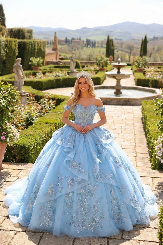 Woman in a blue layered ruffled ball gown with embroidery and tiara in a formal garden