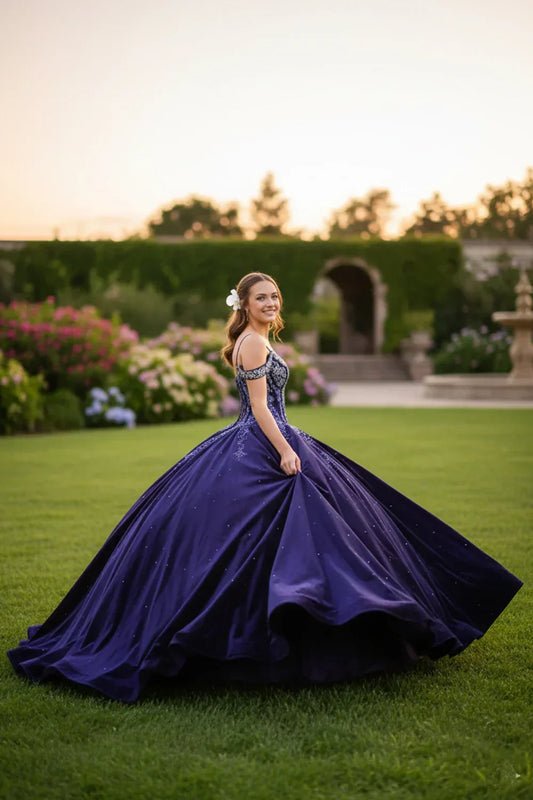 Young woman in a sparkling navy blue ball gown with lace details, posing outdoors at sunset.